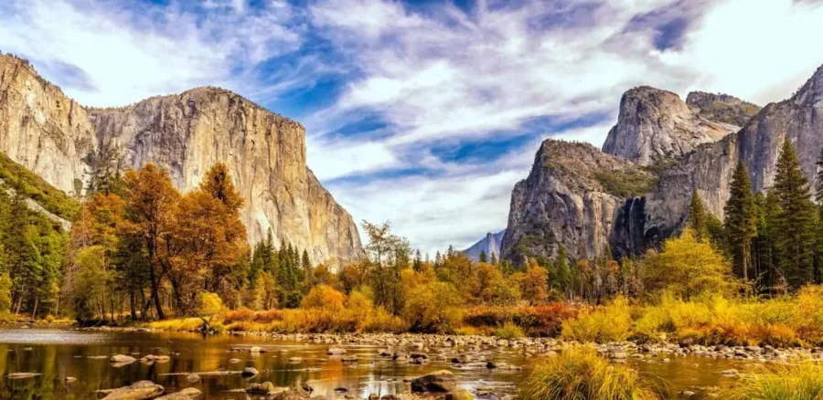 A picturesque view of a rocky lake with yellowish green trees in the background, with huge rocky mountains. View from Yosemite National Park, California.