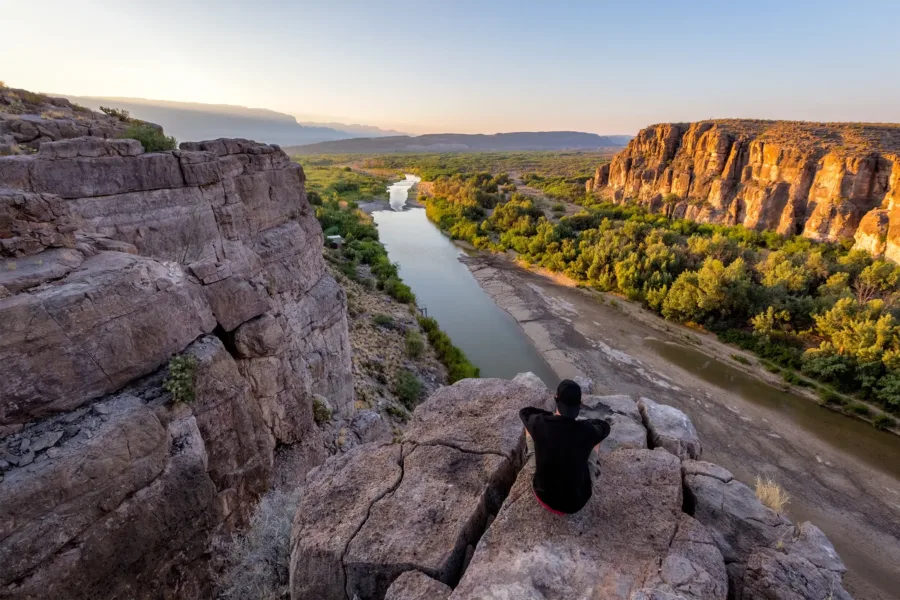 A man sitting on a rocky mountain watching a river flowing